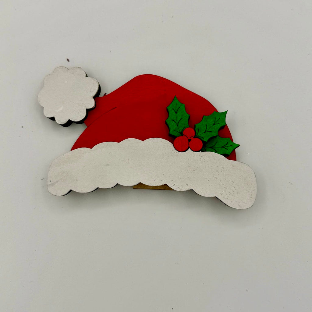 Decorative Christmas ornament with a red Santa hat, white beard, and holly leaves on a light gray background.