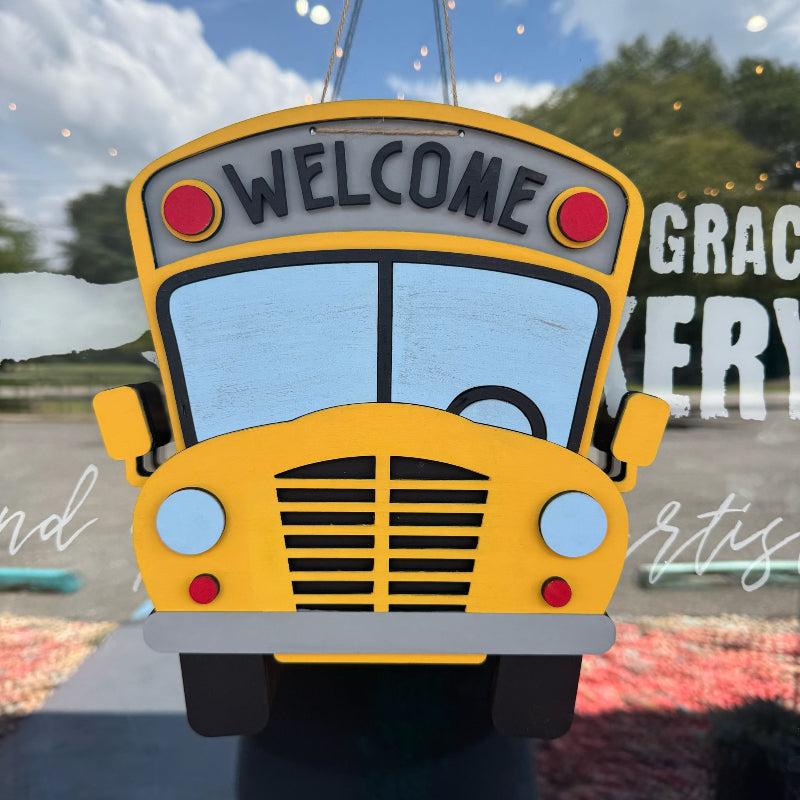 Yellow school bus-shaped sign with 'WELCOME' on a reflective surface.