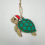 A wooden turtle Christmas ornament painted with a teal green shell, light brown legs, and a red Santa hat, hanging from a natural jute twine string against a plain white background.