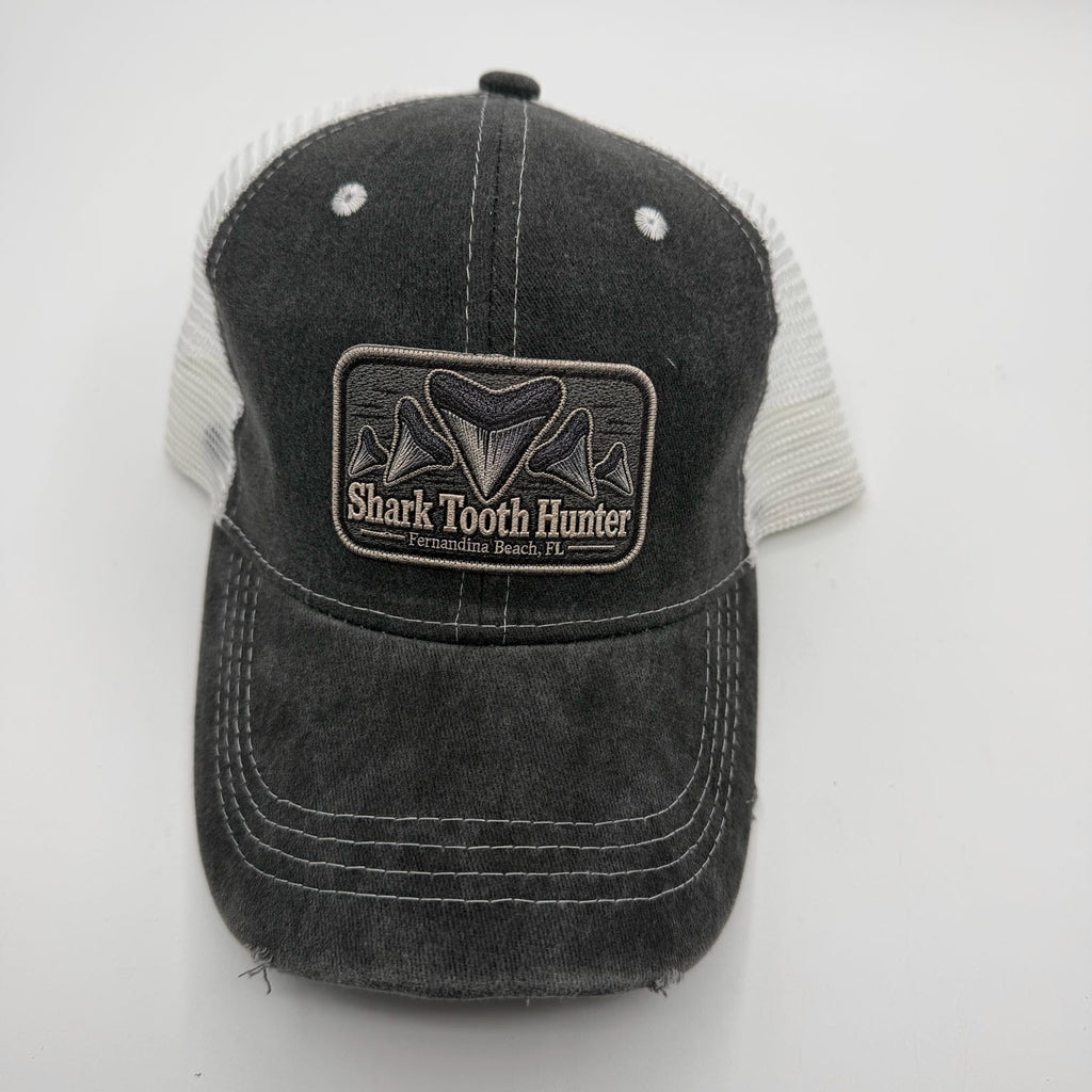 A dark gray washed trucker hat with a black and white Shark Tooth Hunter patch on the front, set against a plain light gray background.