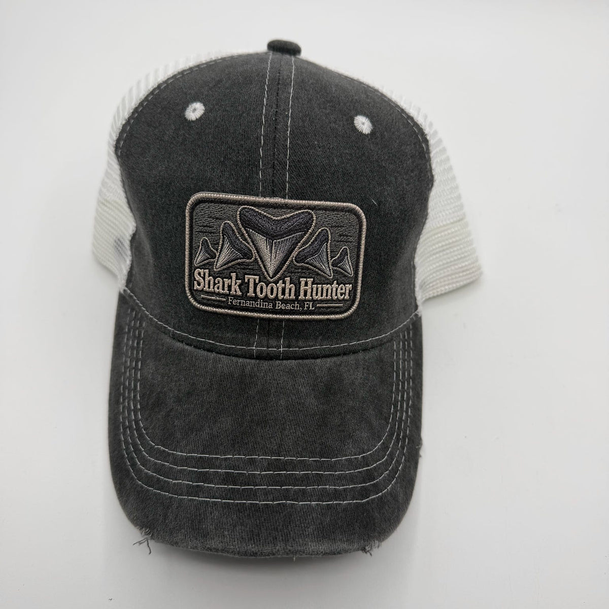 A dark gray washed trucker hat with a black and white Shark Tooth Hunter patch on the front, set against a plain light gray background.