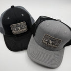 Two trucker hats on a light gray background, one black and one heather gray, both with a rectangular front patch reading Shark Tooth Hunter.