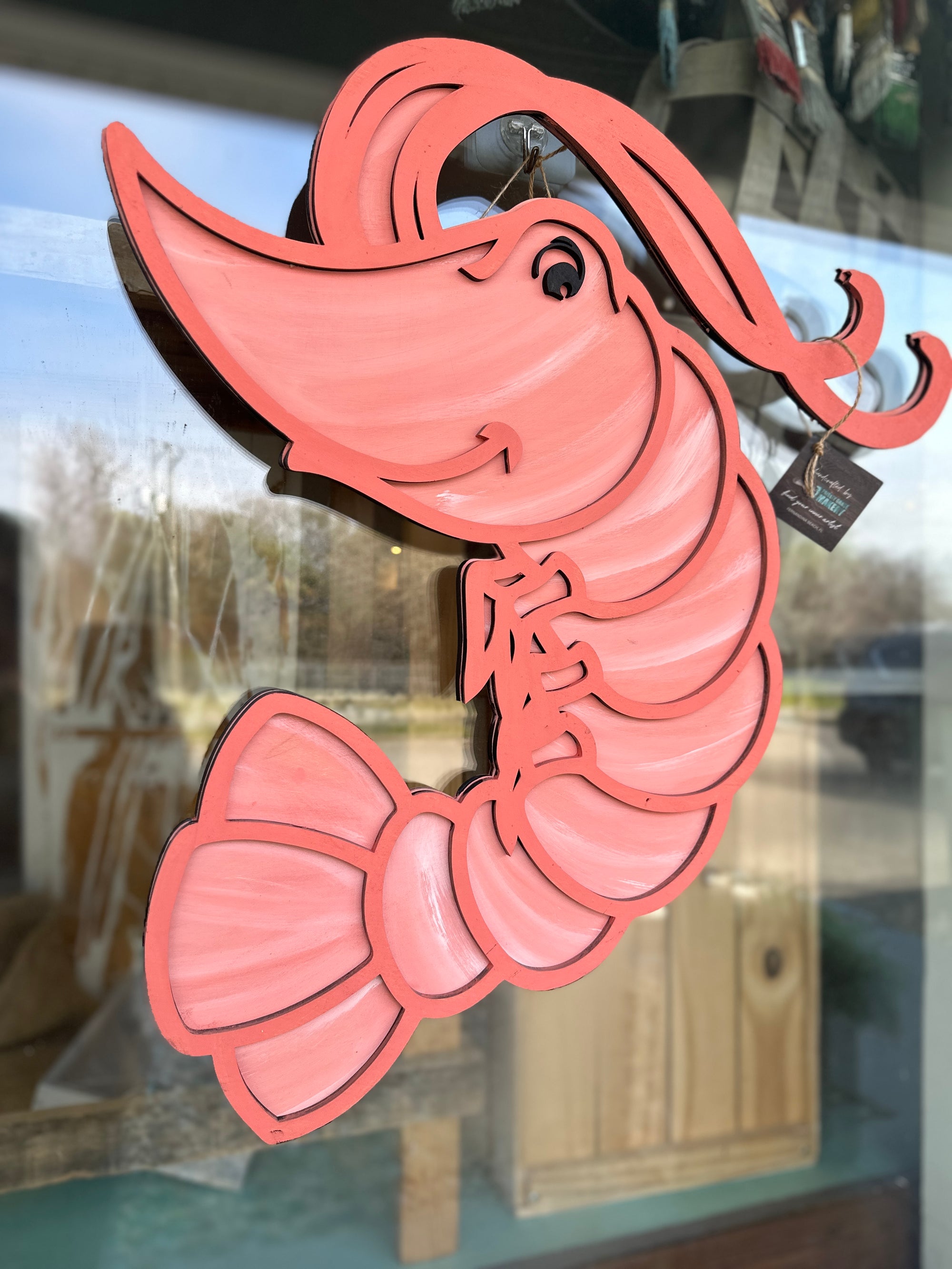 A red-colored wooden door hanger in the shape of a shrimp with decorative elements.