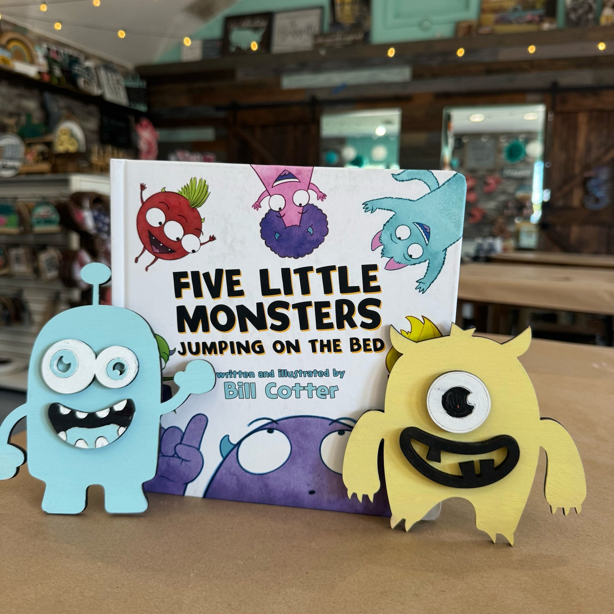 Children's book titled 'Five Little Monsters Jumping on the Bed' with monster character toys on a table.