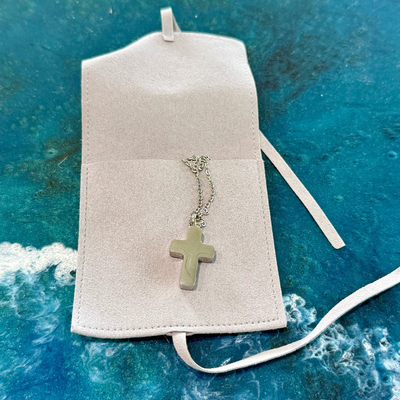 Necklace with a cross pendant on a white pouch against a blue textured background