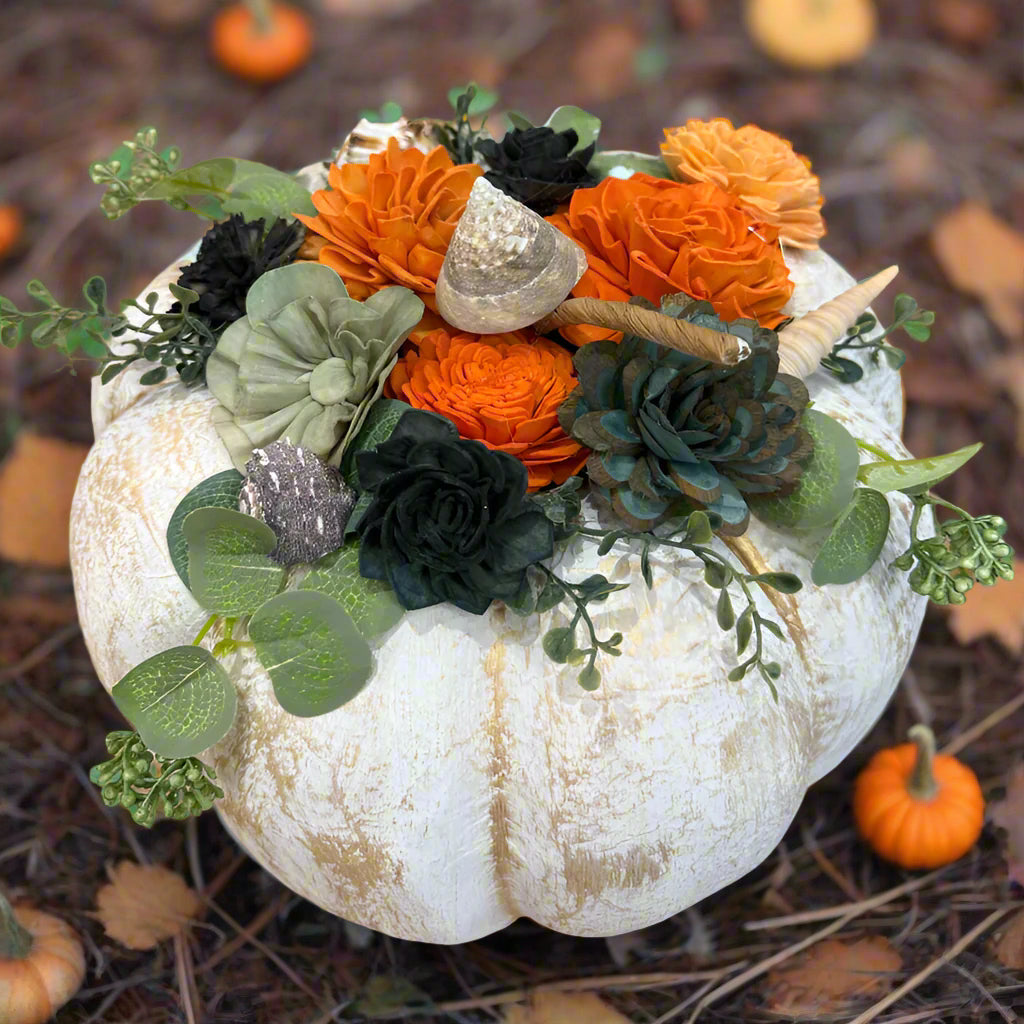 Decorative white pumpkin with orange and black flowers on a table with craft supplies.