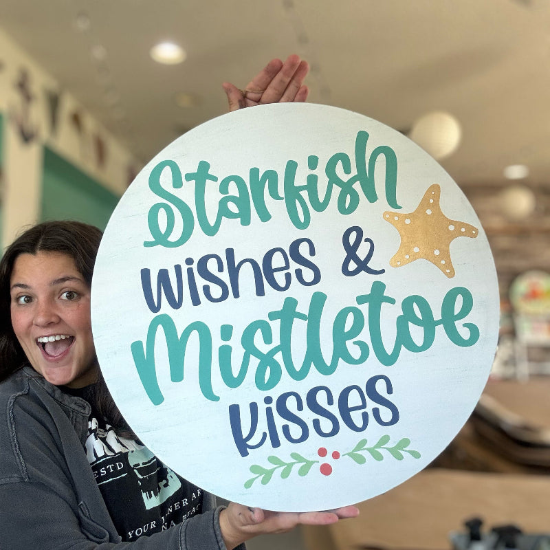 Person holding a round sign with 'Starfish wishes & Mistletoe kisses' text and starfish design.