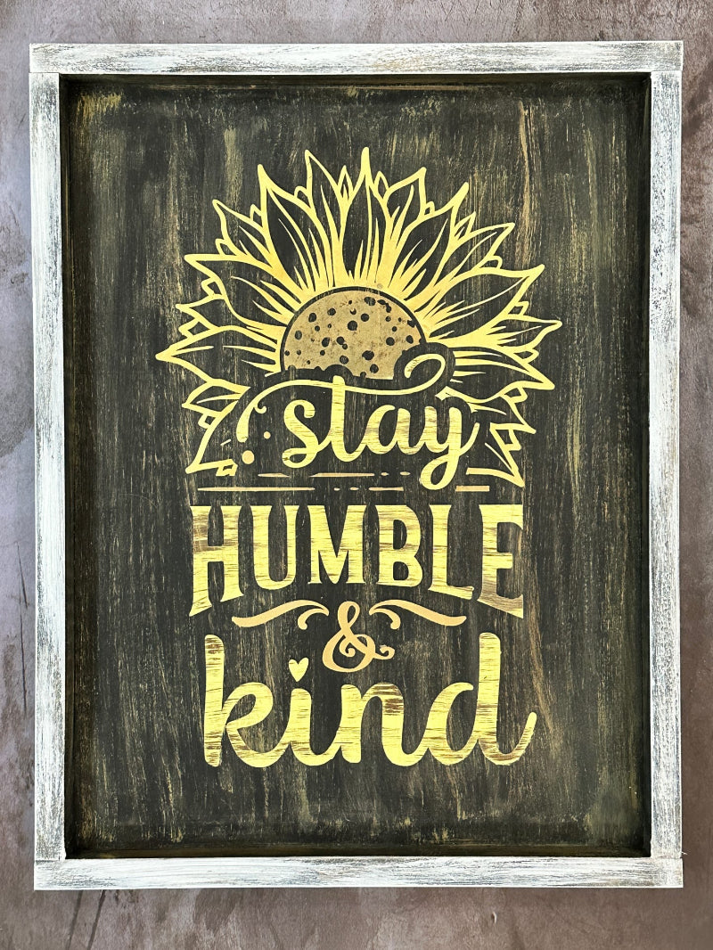 A wooden frame sign with a sunflower design and the text 'stay HUMBLE & kind'.