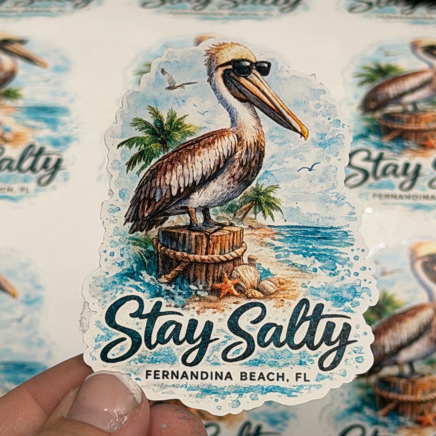 Sticker with a pelican design and 'Stay Salty' text held by a hand, with multiple stickers in the background. Fernandina Beach Local Sticker
