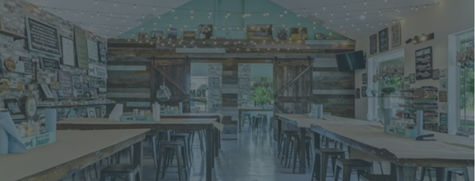 Large room with wooden tables and stools, decorated with various items on the walls.