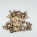 A laser-cut wooden decorative plaque featuring a stylized cow face surrounded by daisies and a small tag that reads 'Turf's Flower in the Bed'.