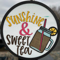 A door hanger with a circular shape featuring a graphic design with text 'Sunshine & Sweet Tea' and an illustration of a tea cup with a lemon slice and a straw.