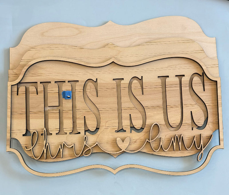 Wooden sign with 'This Is Us' and names on a blue background