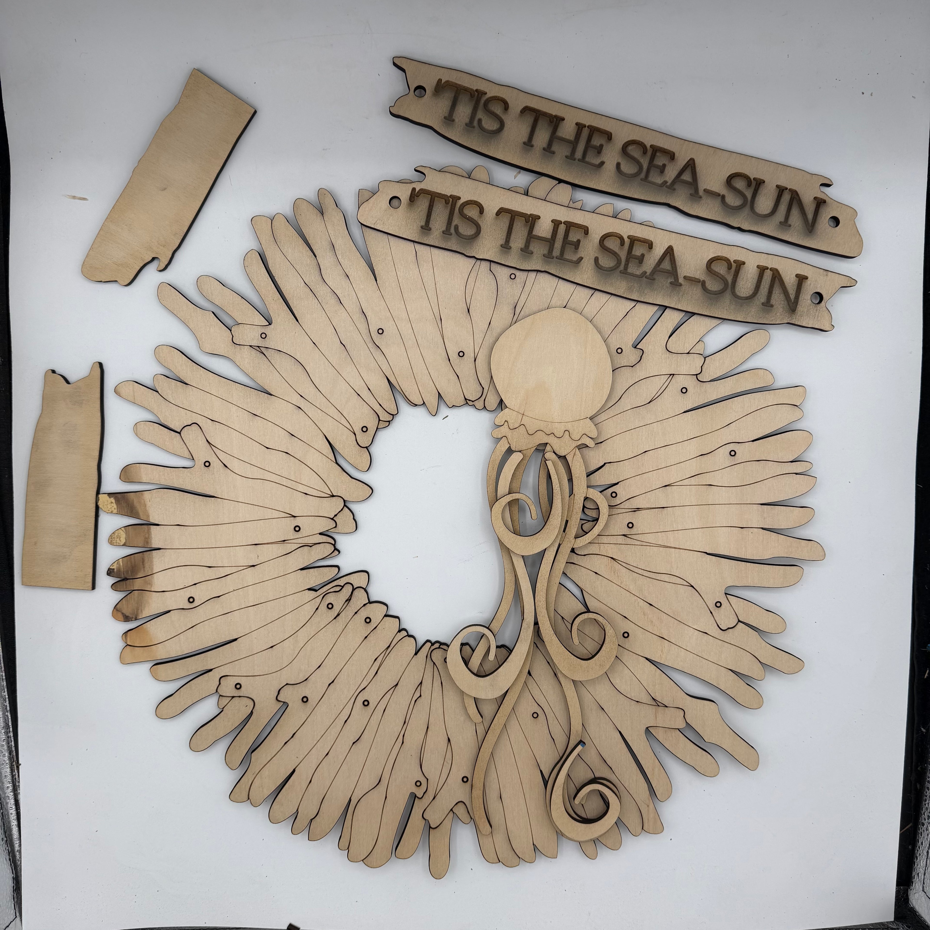 Laser-cut wooden nautical wall decor set featuring a circular sun and moon wreath with an octopus, two banner signs reading 'TIS THE SEA-SUN', and two small rectangular pieces, all shown on a white background.
