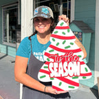 Person holding a decorative Christmas tree sign in front of a building