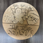 Wooden round decorative item with Christmas-themed cutouts and 'Tis the Season' text on a wooden surface.