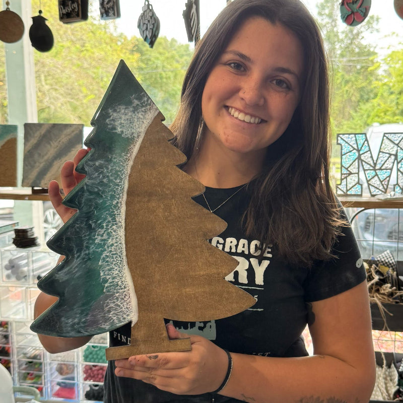 Woman holding a wooden cutout of a dinosaur shape in a workshop setting.