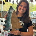 Woman holding a wooden cutout of a dinosaur shape in a workshop setting.