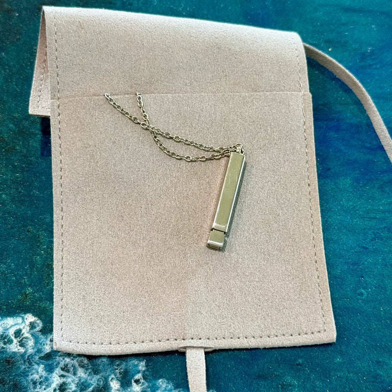 Necklace with a pendant on a beige pouch against a blue textured background