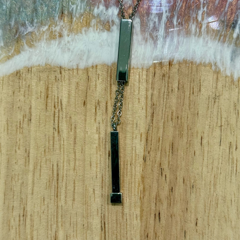 Two silver bar pendants on a chain against a wooden background