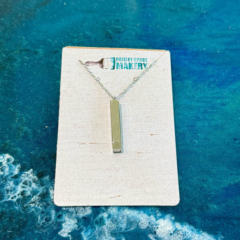 Necklace with a rectangular pendant on a branded card against a blue textured background