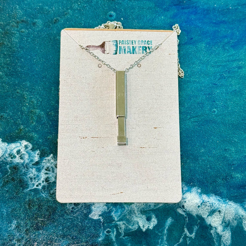 Necklace with a rectangular pendant on a branded card against a blue water background