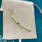 Gold necklace with two rectangular pendants on a beige jewelry pouch against a blue textured background