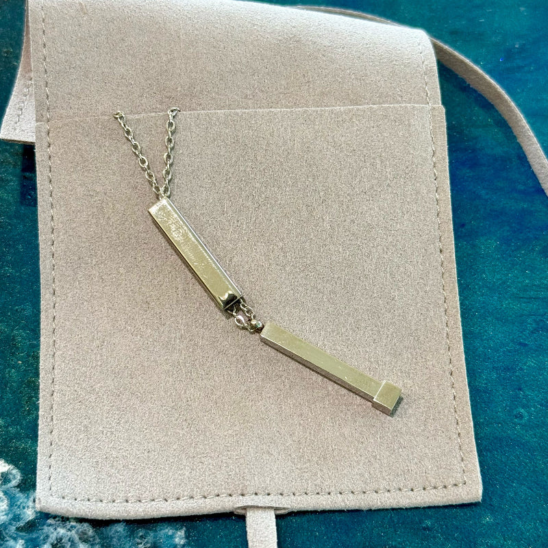 Gold necklace with two rectangular pendants on a beige jewelry pouch against a blue textured background