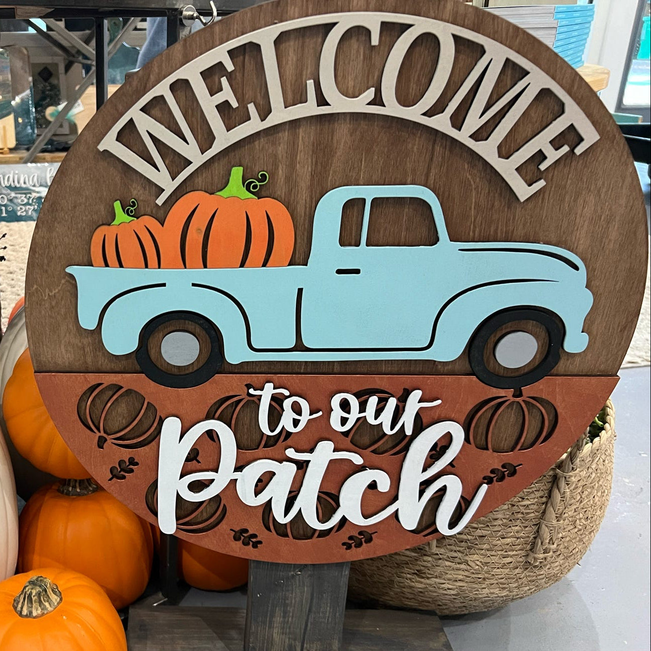 A round door hanger with a wooden background featuring a truck and pumpkins, with the text 'Welcome to our PATCH'.