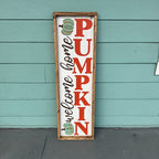 Decorative sign with 'Welcome Home Pumpkin' text against a teal wooden wall.