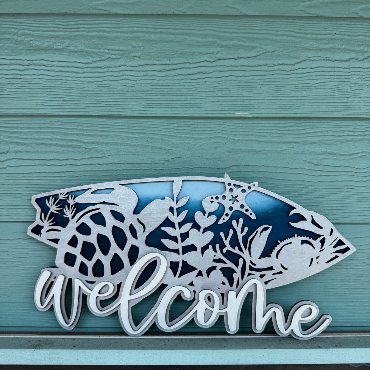  'welcome' sign with marine life design on a teal wooden background