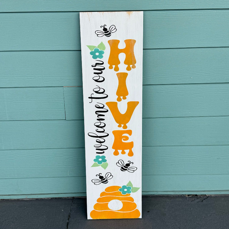 Wooden sign with 'Welcome to our HIVE' text and bee illustrations against a teal background