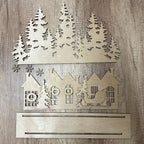 Wooden cutout of a winter scene with houses, trees, and a sleigh on a wooden background