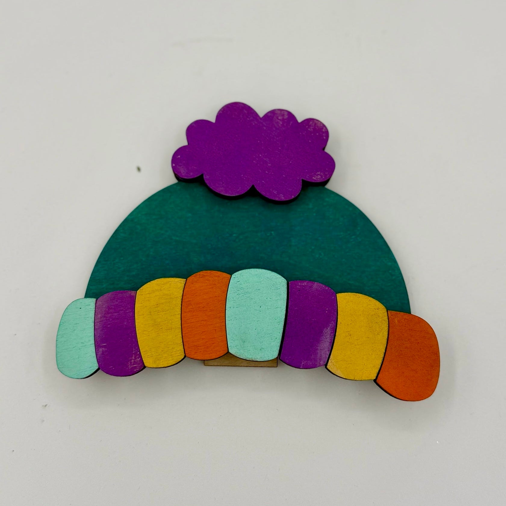 Colorful wooden brooch shaped like a beanie with a rainbow pattern on a white background