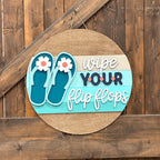 Decorative sign with flip flop design and text 'wipe YOUR flip flops' on a wooden background