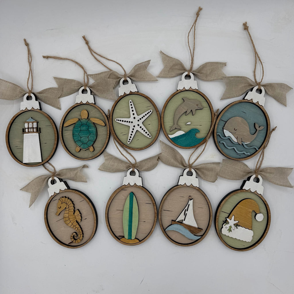 A set of nine oval wooden hanging ornaments with burlap ribbon bows, each featuring a different nautical or beach-themed laser-cut design including a lighthouse, turtle, starfish, dolphin, whale, seahorse, surfboard, sailboat, and Santa Claus.