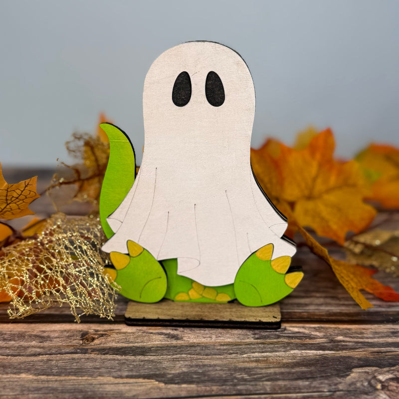 Wooden ghost decoration with green feet on a wooden surface with autumn leaves.