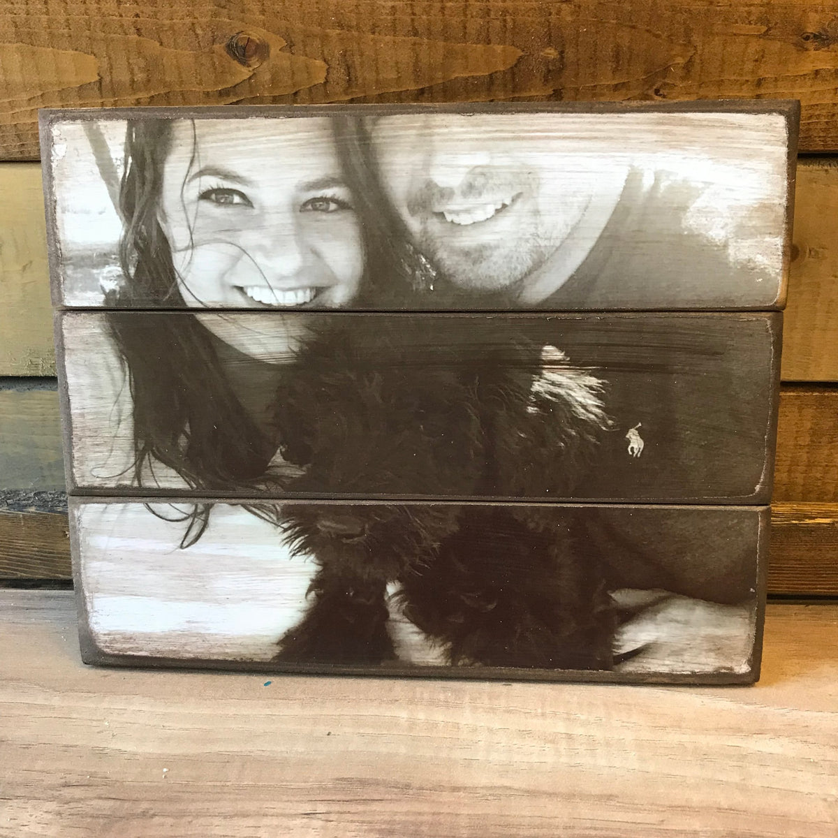 Black and white photo of a smiling couple and their dog on a three plank wood photo block