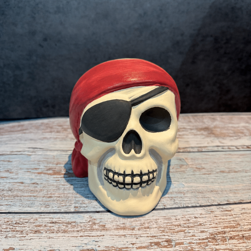 Pirate skull figurine with a red bandana on a wooden surface